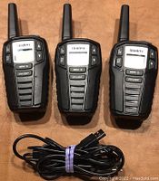 Front view of three Uniden two-way radios with digital displays, buttons, and antennae, along with a bundled USB charging cable below them.