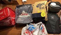 Overview photo showing several cooler bags with Coors Light, Corona Extra, and other brand logos on a table.