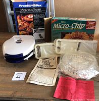 Shows Proctor Silex waffle iron, Micro-chip microwave potato chip maker trays, manuals, and original boxes on a table.