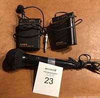 Photo showing front sides of Azden wireless transmitter and receiver units with handheld microphone and MaxSold lot number card.