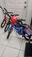 Three kids bicycles pictured together: a red bike with training wheels, a blue Spiderman bike with attached balloon, and a black Panther bike