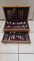 Full view of wooden flatware box with two drawers, top drawer contains Prestige flatware pieces arranged, bottom drawer contains random stainless steel flatware pieces.