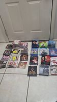 Overview of various new Blu-ray and CD cases spread on floor showing many different titles and duplicates.