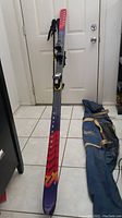 Pair of K2 Triaxial 5500 skis with Tyrolia bindings and vintage Lake Placid ski carry bag on tile floor