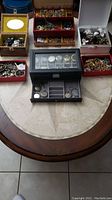 Overview of multiple jewelry storage boxes filled with assorted costume jewelry and watches on a table, showing variety and quantity of items