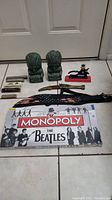 Photo shows unopened Beatles Monopoly game, vintage harmonicas laid out, cast iron nutcracker figure, and pair of Aztec stone bookends.