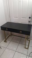 Desk positioned near door showing overall height and depth, black top and gold legs