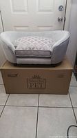 Front view of the gray pet sofa with a geometric-patterned cushion, placed atop the box it came in.