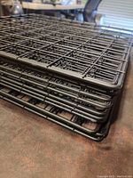 Stacked view of multiple black metal mesh shelves showing edges and thickness