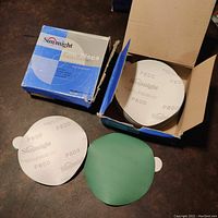 Box containing white circular sanding discs with P600 grit markings and Sunmight branding, stacked inside an open box.