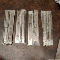 Four packs of metal drawer slides, two slides per pack, total eight in clear plastic packaging on a dark surface.