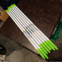 Photo of six white extendable telepoles with bright green ends laid out on a table.