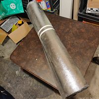 Top view of the rolled sound deadening material stored on a table, showing the rolled silver reflective surface with tape securing it.