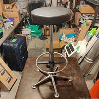Full view of the architect stool showing the black cushioned seat, chrome plinth with five-star base, and adjustable footrest ring.