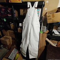 Full view of white Dickies painter's overalls hanging, showing overall shape and pocket details.