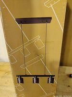 Photo of the hanging lamp fixture assembled and standing upright, showing the rectangular ceiling mount and the three mosaic patterned light shades hanging from cords.