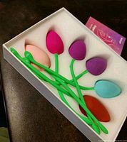 Six colorful kegel balls laid out in a white tray showing different colors and weights with green flexible stems for pelvic floor exercise.