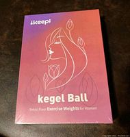 Front view of the unopened factory sealed box of iskeepi Kegel ball kit in gradient pink and peach, featuring minimalist female illustration and floral outline.