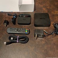 Two Android-based media players with accessories on a brown surface, including one remote control, two power adapters, and one HDMI cable