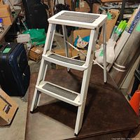 White metal three-step foldable step stool with anti-slip pads on steps, shown from angled front.