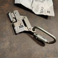 Cable grab device with original packaging visible in background, showing metal body with lever locking mechanism and North brand label.