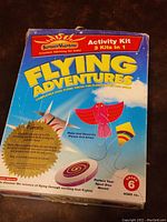 Front packaging of the Flying Adventures kit showing 3-in-1 activity themes: paper airplane, kite, and sport disc, labeled for ages 10+ and grade 6+