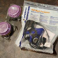 Full lot image showing respirator mask in sealed original package and two separate purple filters.