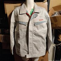 Front view of the light gray Toyota Japan factory uniform jacket with red 'TOYOTA' embroidery on chest and dual chest pockets with gray flaps.