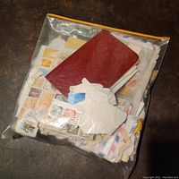 A sealed plastic bag containing a large quantity of various stamps, envelopes, folders, and some brown and red cover booklets or folders.