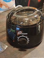 Black Kriorand wax warming pot with clear lid and temperature control dial on a surface
