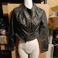 Front view of a black leather cropped jacket on a mannequin showing the diagonal zipper and fitted style.