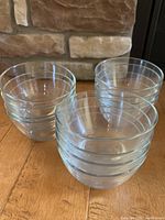 Set of 12 clear glass bowls stacked and grouped on a wooden surface near stone wall background showing size and quantity.