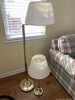 Both lamps shown side by side near a window and plaid upholstered chair on wood floor.