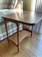 Side view of vintage solid wood drop leaf side table, showing turned legs, lower shelf, and unfolded tabletop.