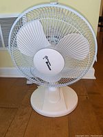 Front view of the white Hawaiian Breeze table fan on wooden floor, showing circular base, fan blades, and grille.