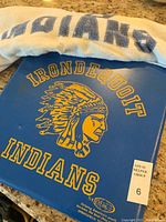 Photo showing white towel with 'INDIANS' lettering and blue stadium seat cushion with Irondequoit Indians logo and text