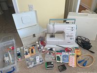 Wide view of Kenmore sewing machine next to sewing box and large assortment of sewing accessories including thread spools, scissors, needles, pins, bobbins and more.