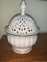 Front view of the Lenox Versailles candle box showing the pierced dome lid with finial and gold trim on white ceramic flared base.