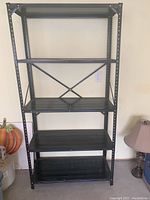 Full front view of black metal storage shelf with five shelves spaced evenly and cross brace back support.