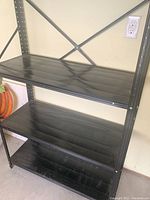 Full view of top and middle shelves of black metal storage shelf against a beige wall, showing horizontal slatted shelf design and metal frame.