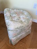 Full view of the semi-circular occassional ottoman in floral upholstery with tufted button detail on top, showing the box pleat skirt covering the base and wheels.