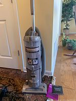 Full view of Shark Navigator Deluxe upright vacuum in light grey with hose attached, positioned on carpet by door. Instruction manual visible at base.