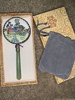 Full view of the hand mirror in box with protective pouch laid beside it