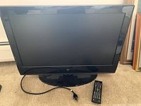 Front view of the Westinghouse 26-inch television showing the screen, base stand, power cord, and remote control placed beside it on the floor.