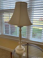 Full view of the white wooden table lamp with fabric shade near window showing overall appearance and scale.