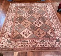 Top-down photo of full rectangular multicolor wool rug with floral and diamond patchwork pattern on wood floor.