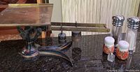 Photo showing full antique kitchen scale with brass weighing platform and black painted metal base with decorative accents.