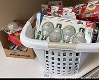 Laundry basket filled with boxed light bulbs, plate covers, and outlet items.
