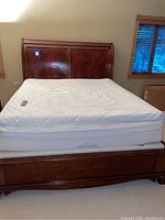 Full view of wooden sleigh bed frame with Sleep Number mattress and box spring on carpeted floor, includes mattress remote on top.