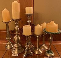Seven metal candlesticks of varying heights holding ivory candles displayed together